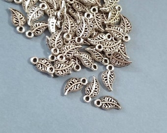 Könnte beinhalten: Ein Haufen silberner Metall-Blätter-Anhänger mit einem zarten, filigranen Design. Die Anhänger haben oben ein Loch zum Anbringen an Schmuck oder andere Bastelarbeiten.