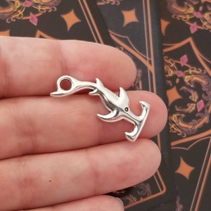 May include: Silver-toned hammerhead shark charm with a loop for attaching to a necklace or bracelet. The charm is detailed with a textured finish and a small hole on the top.