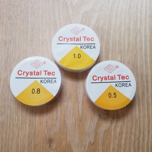 May include: Three white spools of clear elastic thread labeled "Crystal Tec Korea" with sizes 0.5, 0.8, and 1.0.