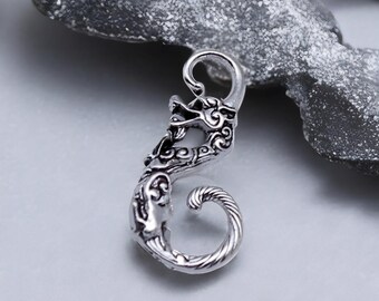 May include: A silver-colored dragon-shaped pendant with intricate details. The pendant features a dragon head with detailed scales and a curled tail. The design is ornate and detailed, with a loop at the top for hanging.