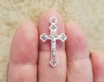 May include: Silver-toned crucifix charm with a detailed figure of Jesus Christ on the cross. The charm has a loop at the top for attaching to a necklace or bracelet.