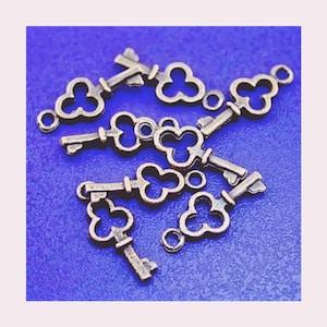 May include: A group of eight antique gold-toned key charms with a clover design. The keys are arranged in a cluster on a blue background.