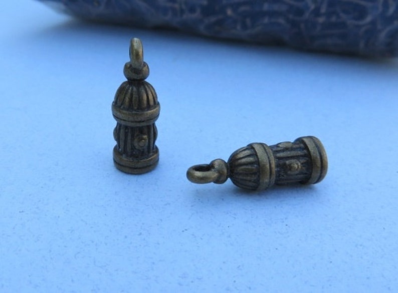May include: Two antique gold-toned metal charms shaped like fire hydrants. The charms have a detailed design and are perfect for jewelry making or crafting.