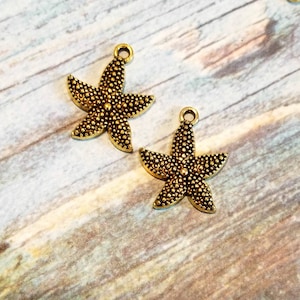 May include: Two gold-tone metal starfish charms with a textured surface. The charms have a loop at the top for attaching to jewelry or other crafts.