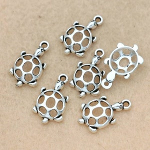 Puede incluir: Un conjunto de abalorios plateados con forma de tortuga. Cada abalorio presenta un dise&ntilde;o hueco y calado en el caparaz&oacute;n y un lazo para sujetarlo a joyas u otras manualidades. Los abalorios son peque&ntilde;os, con una cabeza y patas de tortuga detalladas.