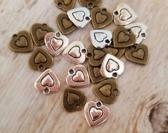 May include: A collection of silver and bronze heart-shaped charms with a double heart design. The charms have a hole at the top for attaching to jewelry or other crafts.