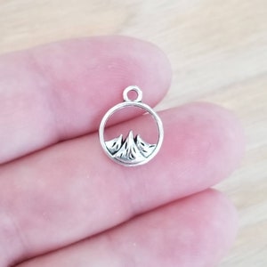 May include: Silver charm with a mountain range design inside a circle. The charm is small and delicate.