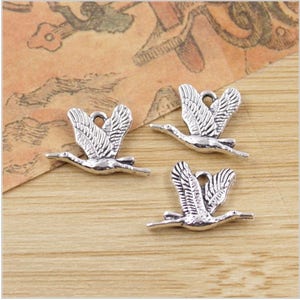May include: Three silver-toned metal charms shaped like flying cranes. The charms have a loop at the top for attaching to jewelry or other crafts.