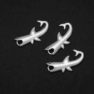 May include: Three silver shark charms with open mouths and a loop at the top for attaching to jewelry or other crafts.