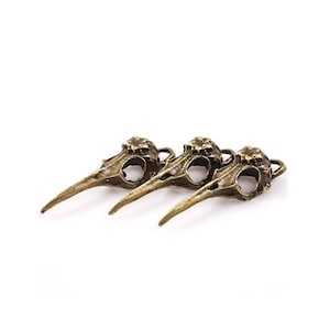 May include: Three antique gold bird skull charms with a flower detail on the top of the skull. The charms have a loop for attaching to jewelry or other crafts.