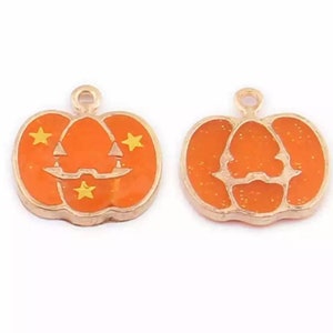 May include: Two gold-colored pumpkin charms with orange enamel. One pumpkin has a jack-o'-lantern face with three gold stars. The other pumpkin has a simple outline of a pumpkin with a gold glitter finish.