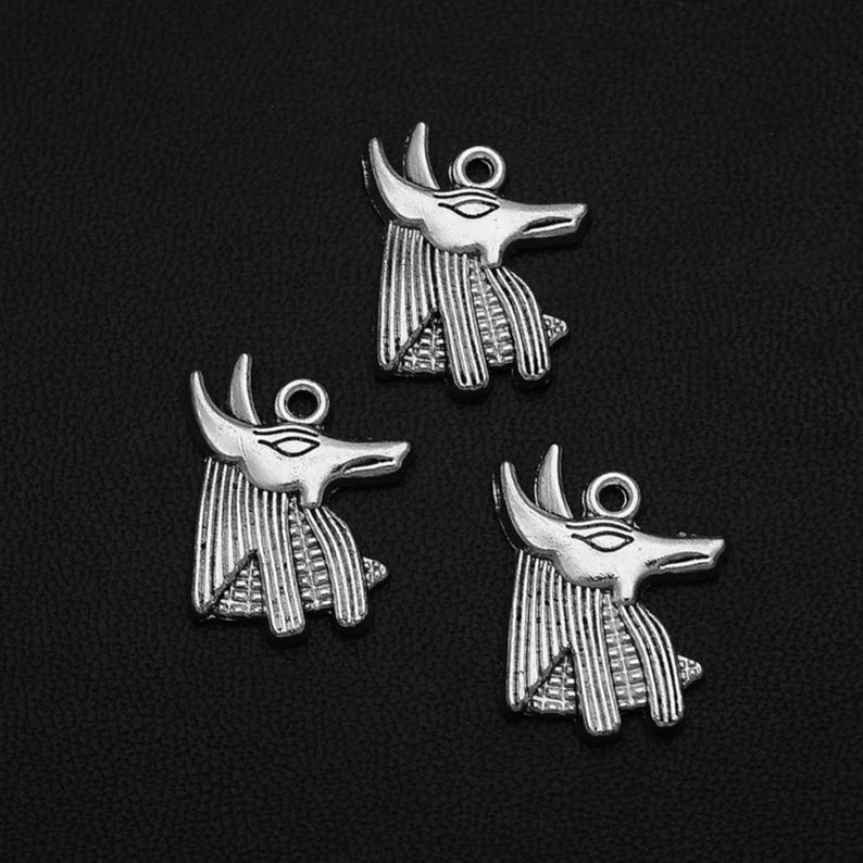 May include: Three silver charm pendants in the shape of an Anubis head. The pendants have a detailed design and are perfect for jewelry making.
