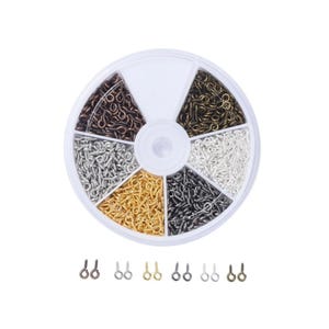 May include: A clear plastic container with a segmented wheel of small eye screws in various metallic finishes: bronze, gold, silver, black, and copper. A row of individual eye screws in matching colors are displayed below the container. Ideal for jewelry making and crafts.