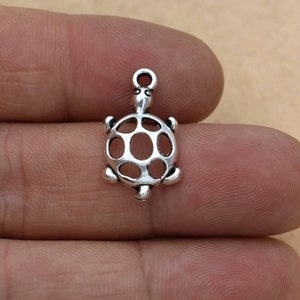 Puede incluir: Un peque&ntilde;o dije de tortuga de color plateado, con un lazo en la parte superior para sujetarlo a la joyer&iacute;a. La tortuga tiene un caparaz&oacute;n detallado con recortes ovalados y peque&ntilde;as patas en forma de aleta. El dije es de metal y tiene un aspecto ligeramente envejecido.