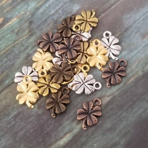 May include: A collection of metal four-leaf clover charms in gold, silver, and bronze finishes. The charms have a loop at the top for attaching to jewelry or other crafts.