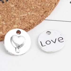 May include: Two silver metal charms, one with a heart design and the other with the word "Love" engraved on it.