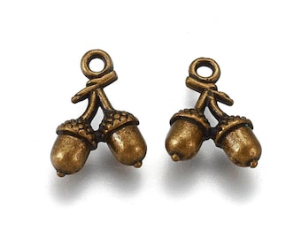 May include: Two antique gold acorn charms with a loop for hanging. The acorns are connected by a stem and have a detailed design.