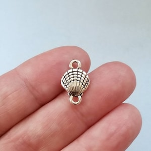 May include: Silver-toned metal seashell charm with two jump rings. The charm is designed to be used as a connector for jewelry making.