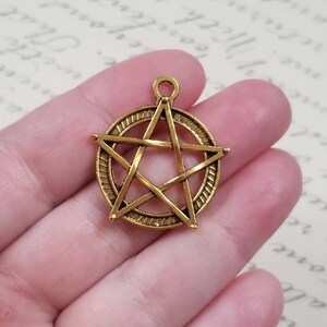 May include: Gold-toned metal pendant charm featuring a five-pointed star with a circle around it. The star is a pentagram, a symbol often associated with witchcraft and paganism.