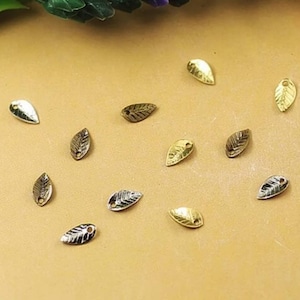 May include: A collection of gold and silver leaf charms with a hole for stringing. The charms are in the shape of a leaf with a detailed vein pattern.