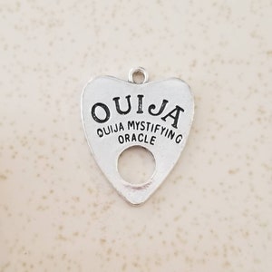 May include: Silver charm in the shape of a heart with the word "OUIJA" written on it. The charm also says "OUIJA MYSTIFYING ORACLE".