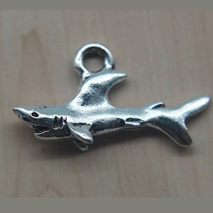 May include: Silver shark charm with a loop for attaching to a necklace or bracelet. The charm is detailed with a fin and a mouth.