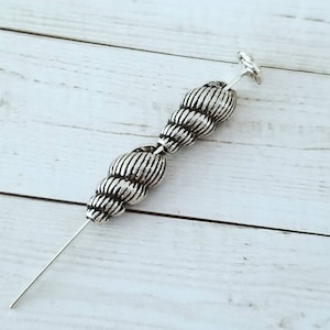 May include: Silver metal beads strung on a silver wire. The beads are round and have a textured surface.