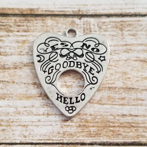 May include: Silver charm in the shape of a heart with the words "YES", "NO", "GOODBYE", and "HELLO" inscribed around a circular opening. The charm has a skull and crossbones design in the center.