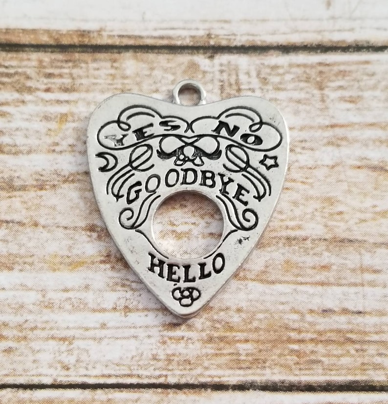 May include: Silver charm in the shape of a heart with the words "YES", "NO", "GOODBYE", and "HELLO" inscribed around a circular opening. The charm has a skull and crossbones design in the center.