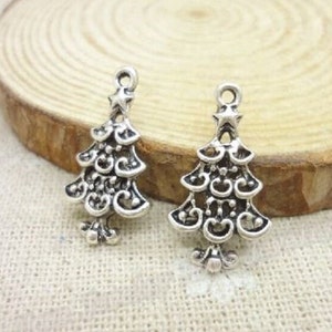 May include: Two silver-toned Christmas tree charms with intricate designs. Each charm features a star at the top and a swirl pattern.