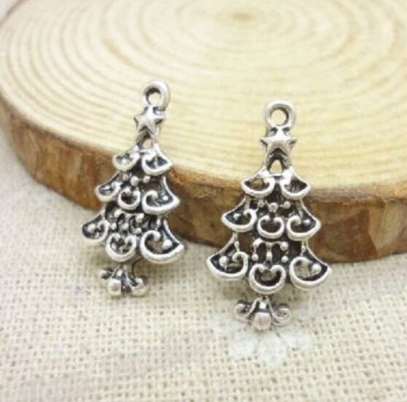 May include: Two silver-toned Christmas tree charms with intricate designs. Each charm features a star at the top and a swirl pattern.