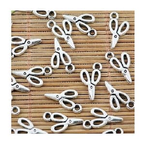 May include: A collection of small, silver-colored scissors charms. The charms are scattered across a bamboo mat, each with a loop for attaching to jewelry or other crafts. The scissors have detailed blades and handles.