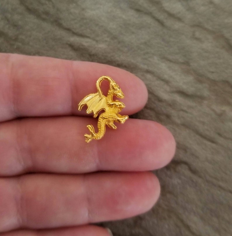 K&ouml;nnte beinhalten: Ein goldfarbener Drachen-Anh&auml;nger mit detaillierten Fl&uuml;geln und einer strukturierten Oberfl&auml;che.