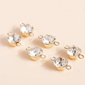 May include: Six gold-toned connector charms with clear crystal rhinestones. Each charm has two loops for attaching to jewelry or other crafts.