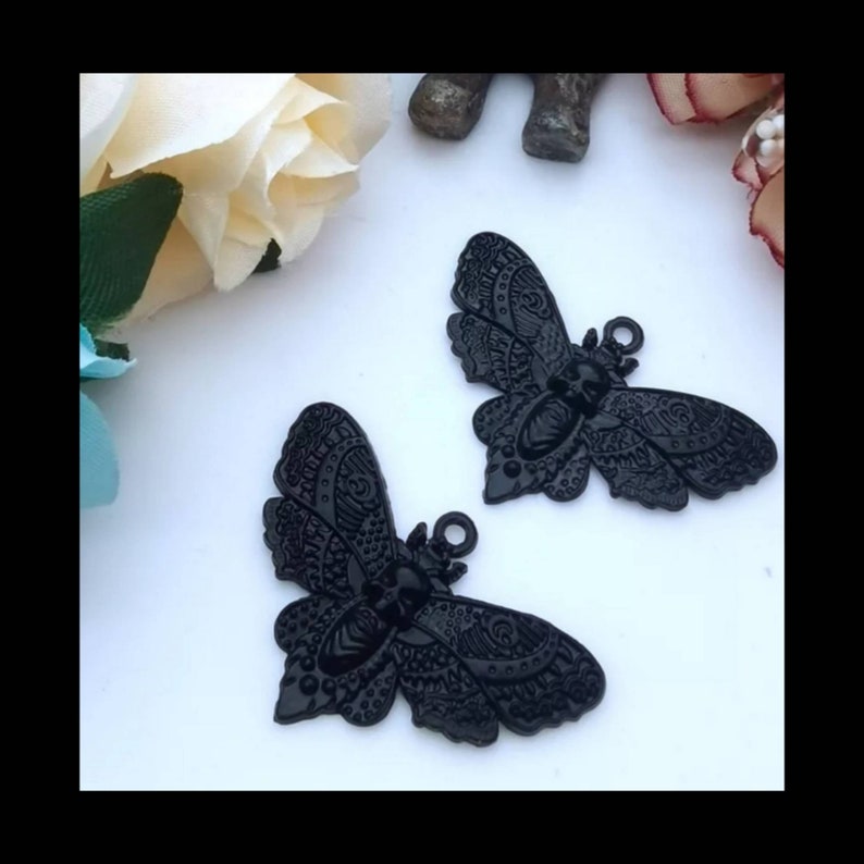 May include: Two black metal butterfly charms with intricate details. The butterflies have a textured surface and a slightly raised design.