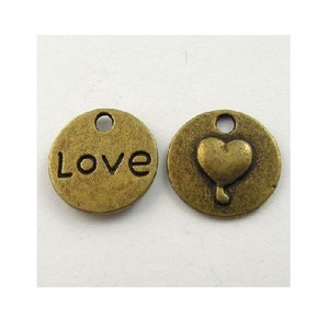 May include: Two antique gold-toned metal charms. One charm has the word "Love" engraved on it. The other charm has a raised heart shape.