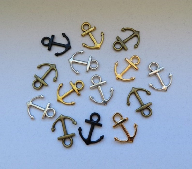 K&ouml;nnte beinhalten: Eine Sammlung von 13 silbernen, goldenen und schwarzen Anker-Anh&auml;ngern. Die Anh&auml;nger sind in einem Kreis auf wei&szlig;em Hintergrund angeordnet.