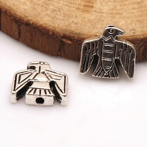 May include: Two silver eagle charms with detailed designs. The charms have a hole for stringing or attaching to jewelry.