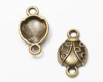 May include: Two antique bronze-colored metal ladybug-shaped jewelry connectors. One piece shows the detailed, embossed back with circular patterns, while the other displays the hollow, smooth interior. Each connector features two small loops.