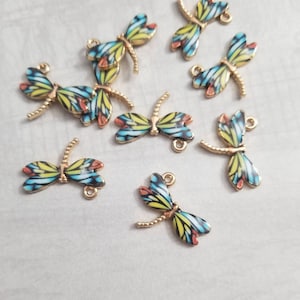 May include: Assortment of eight gold-tone dragonfly charms with blue, yellow, and red enamel details. The dragonfly charms have a beaded wire tail and a loop for attaching to jewelry.