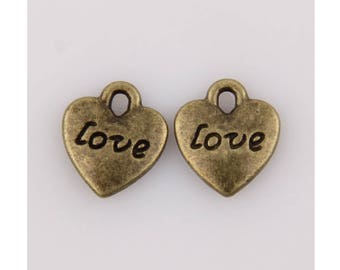 May include: Two bronze-colored heart-shaped charms. Each charm has the word "love" inscribed on it. The charms have a loop at the top for attaching to a necklace or bracelet. The background is a solid, off-white color.