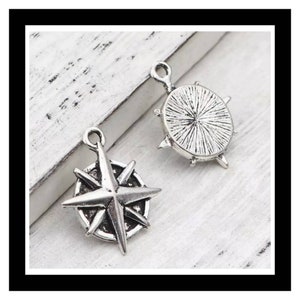May include: Two silver charm pendants, one shaped like a compass with a star in the center, and the other a round compass with a textured surface.