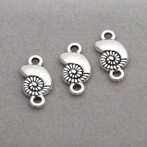 May include: Three silver-toned metal charms in a seashell design. Each charm features a spiral center and a loop at the top and bottom for attaching to jewelry or other crafts. The charms are displayed on a gray background.