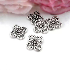 May include: Five silver metal flower-shaped charms with intricate designs. Each charm has a center circle with smaller circles around it, and four swirls extending from the center.