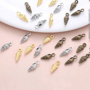 May include: Assortment of silver, gold, and bronze seashell charms with a loop for hanging. The charms are scattered on a pink surface.