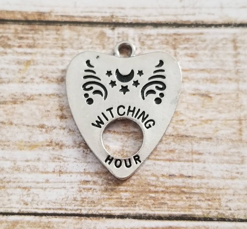 May include: Silver charm in the shape of a heart with the words "Witching Hour" and a crescent moon and stars design.