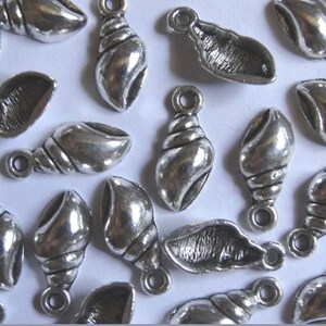 May include: A collection of silver-toned metal seashell charms with a loop for attaching to jewelry or crafts.