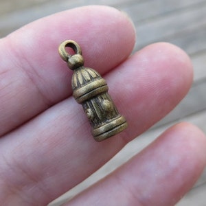May include: A small, antique gold-colored metal charm shaped like a fire hydrant. The charm has a loop at the top for attaching to a necklace or bracelet.