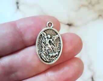 May include: Silver charm featuring a depiction of Saint Michael the Archangel, with the words "St. Michael" inscribed around the edge.