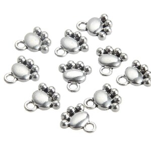 May include: Ten silver-toned metal charms shaped like a paw print with five small beads around the edge. Each charm has a loop at the top for attaching to jewelry or other crafts.
